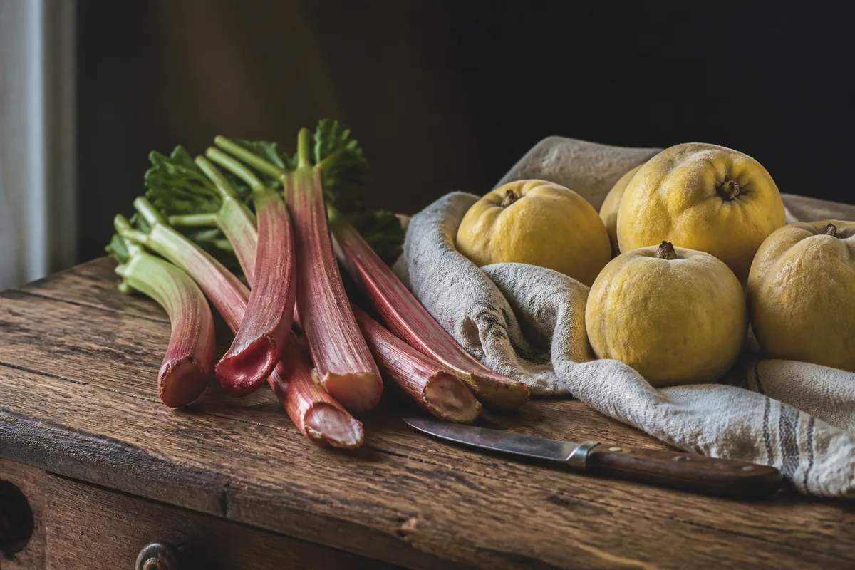 Tiges de rhubarbe et coings posés sur une table en bois dans une cuisine de ferme